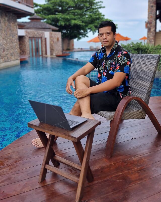 ภัทรชัย ไชยมงคล นั่งทำงานกับแล็ปท็อปบนระเบียงไม้ริมสระว่ายน้ำ